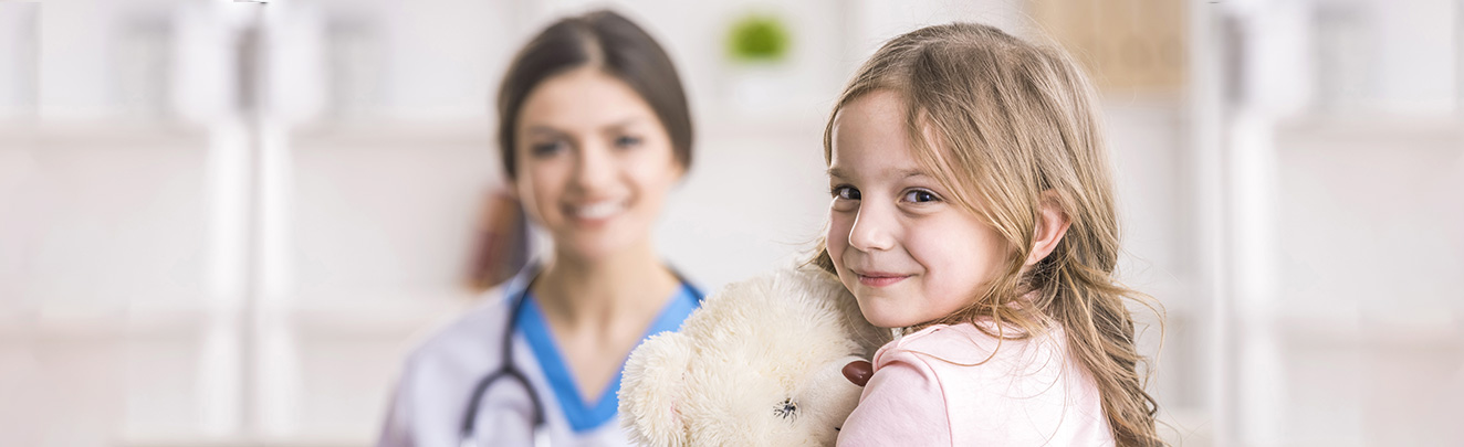 Uma criança segurando um urso de pelúcia com uma médica ao fundo
